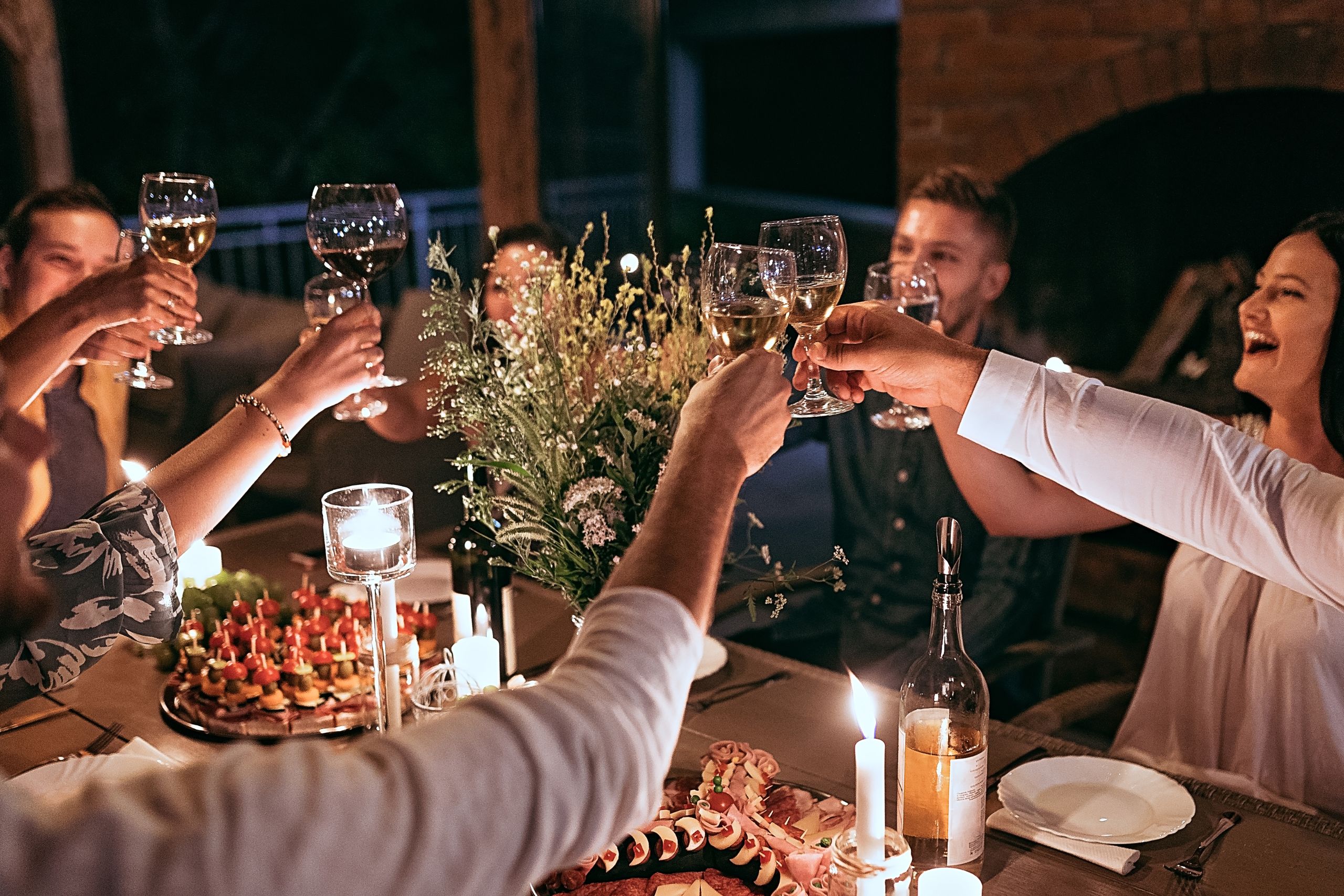 people around a table cheering wine glasses and enjoying outdoor entertainment enhanced by a porch screen